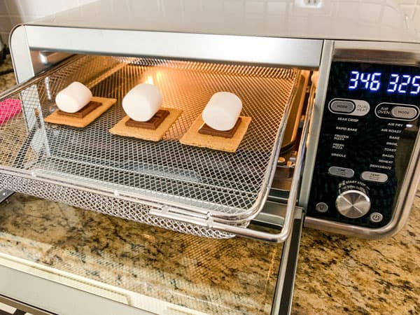 Graham crackers topped with chocolate and marshmallows in an air fryer oven basket.