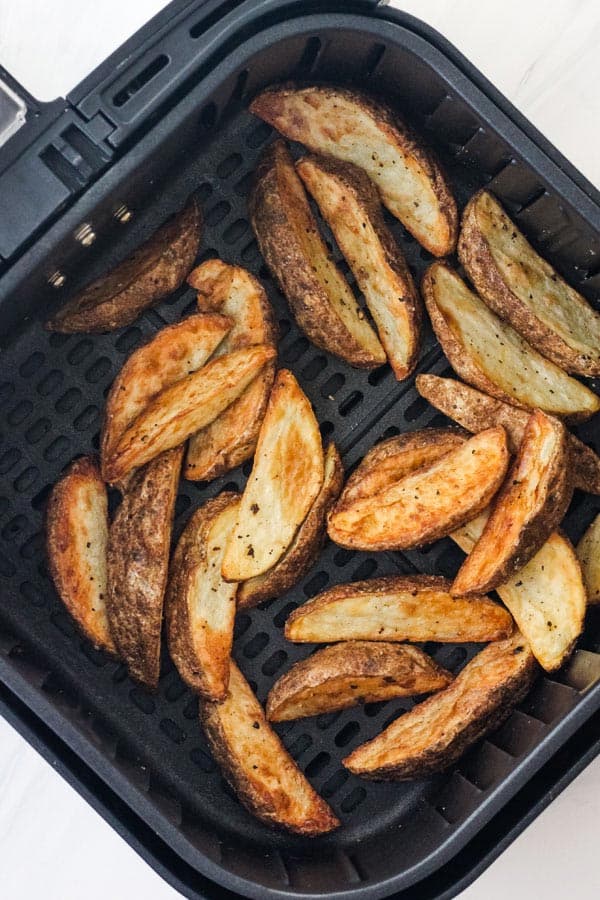 Overhead view of browned potato wedges in an air fryer basket.