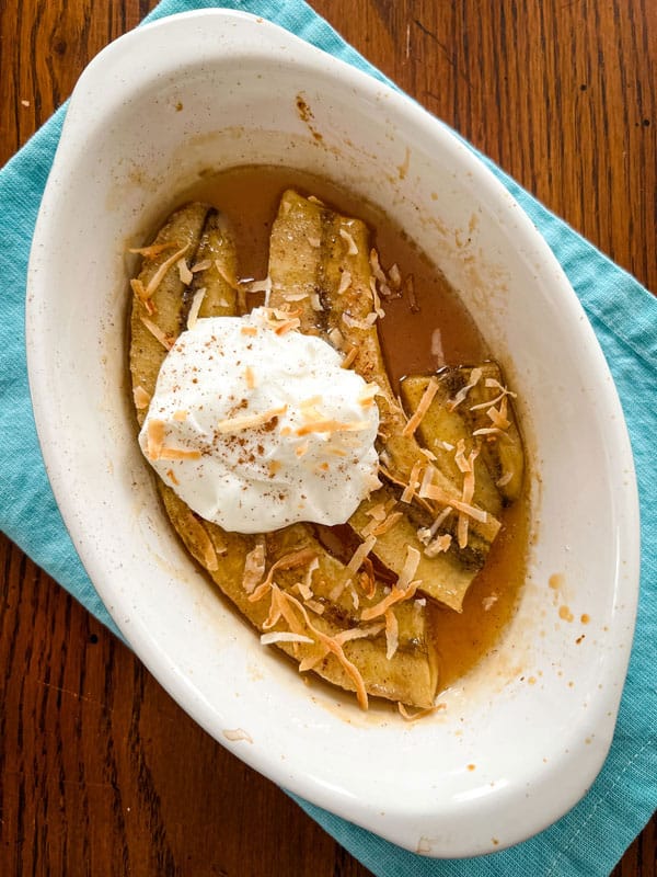 Baked banana halves in a gratin dish with yogurt and toasted coconut.