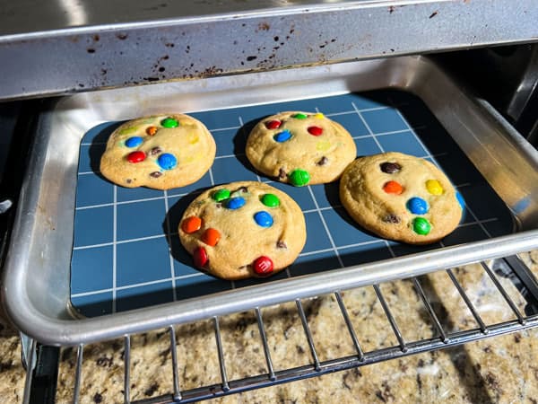 Pan with cookies and flat-laying mat inside toaster oven.