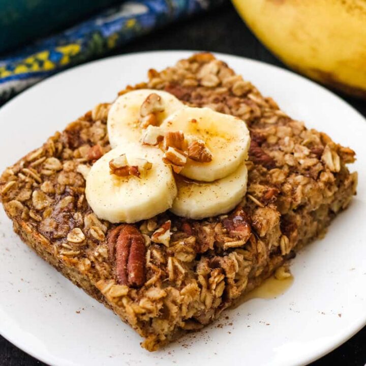 Baked oatmeal on plate topped with banana slice and drizzle of maple syrup.