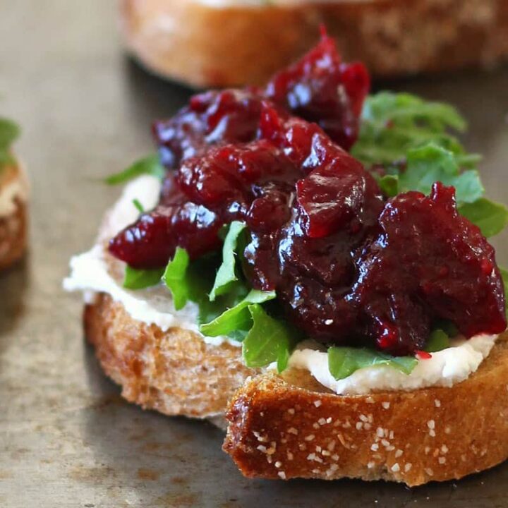 Closeup of crostini topped with goat cheese, arugula, and balsamic roasted cranberries.