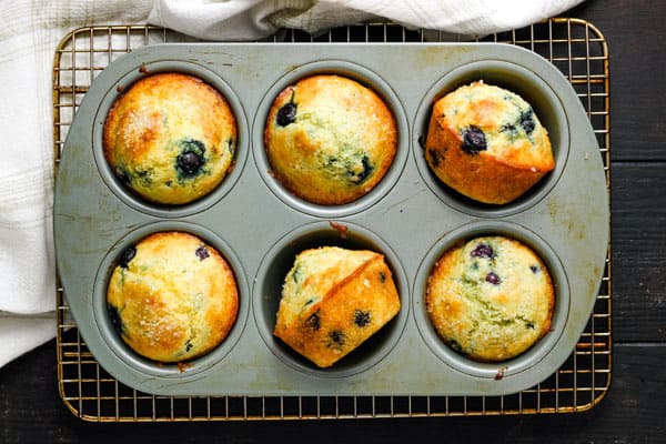 Overhead view of golden blueberry corn muffins cooling in a pan.