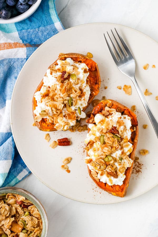 Overhead view of sweet potato halves on a plate topped with cottage cheese and granola.