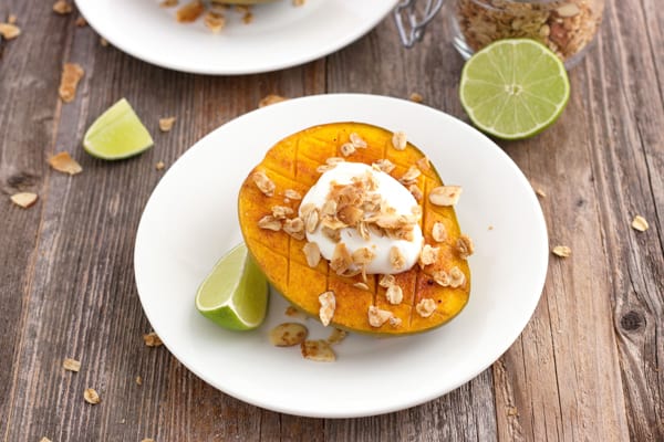 A white plate with half a mango on a wooden table.