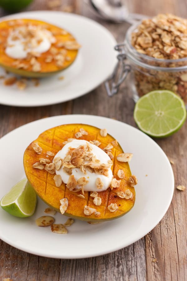 Mango halves on white plates with lime wedges and granola.