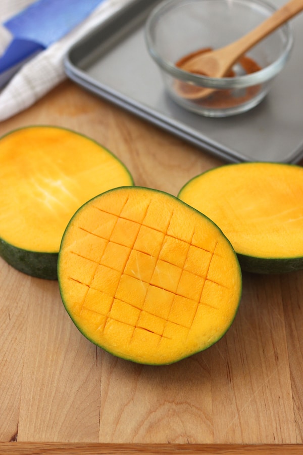 A cutting board with mango sliced in half and scored in a crosswise pattern.