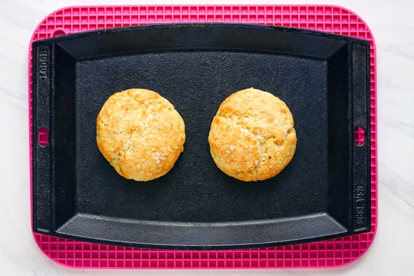 Overhead view of baked biscuits on a small cast iron griddle.