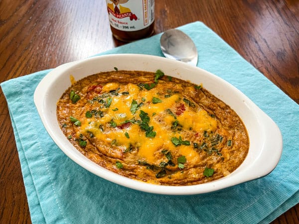 Gratin of baked eggs on a blue napkin next to a bottle of hot sauce.