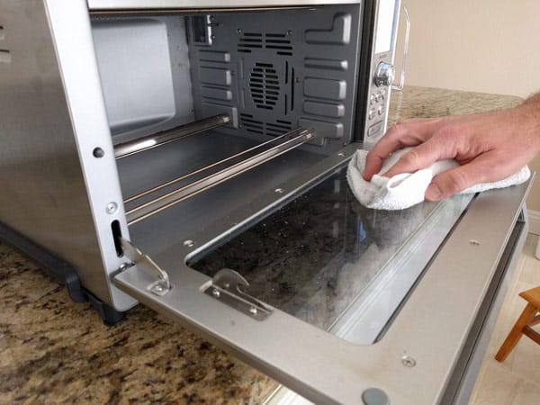 Hand using a rag to clean toaster oven glass door.