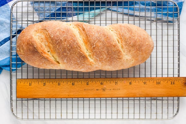 Small loaf of bread cooling on a rack next to a ruler measuring 9 inches long.