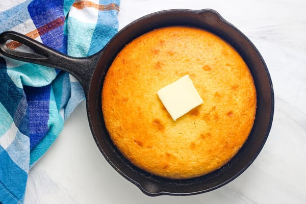 Golden baked cornbread in an 8-inch skillet topped with a pat of butter.