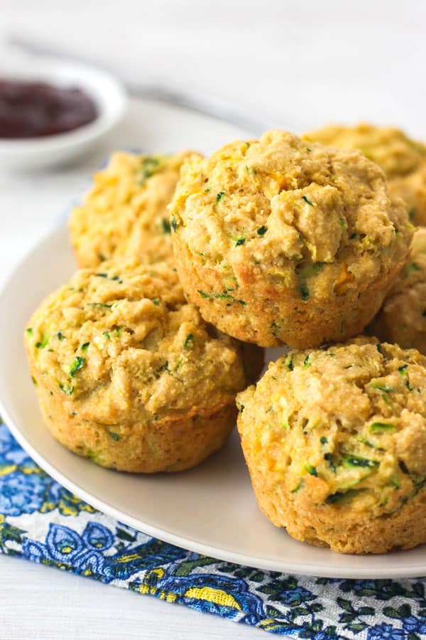 Cornbread zucchini muffins stacked on a tan plate on top of a blue paisley napkin.