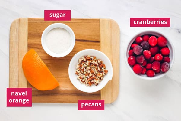 Ramekins of sugar, pecans, cranberries, and a quarter of an orange arranged on a countertop.