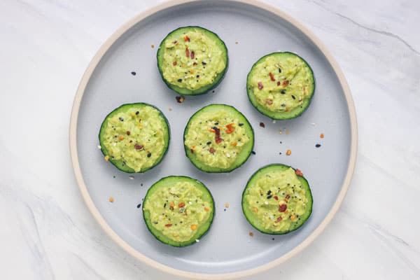 A plate of cucumber slices topped with mashed avocado and seasoning.
