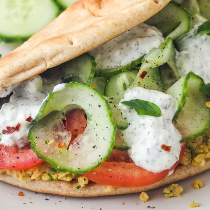 Closeup of folded pita filled with mashed chickpeas, cucumber ribbons, and sliced tomatoes.
