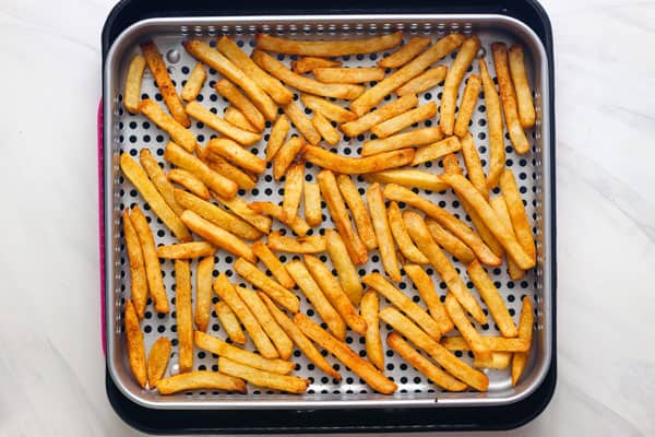 Seasoned fries baked on an air fryer basket set in a pan.