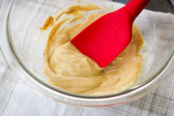 Seasoned yogurt in a glass bowl with a red spoon.