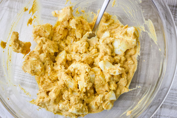 Mashed egg salad in a glass bowl on a white towel.