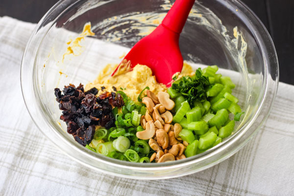 A glass bowl with mashed eggs, green onions, cashews, and sliced celery.