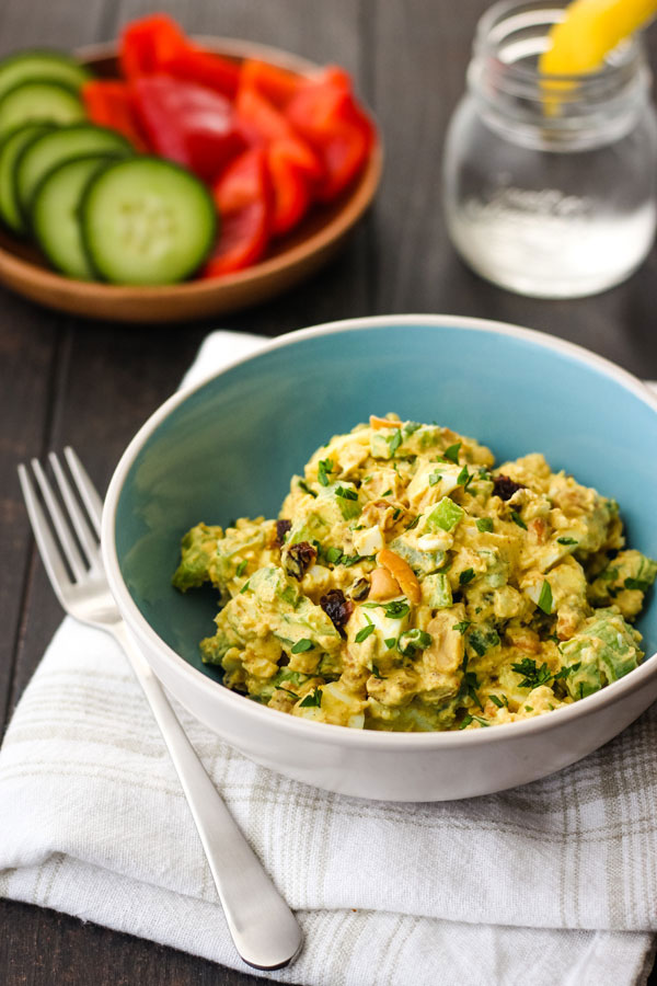 Egg salad in a blue bowl on a white napkin with a plate of veggies.