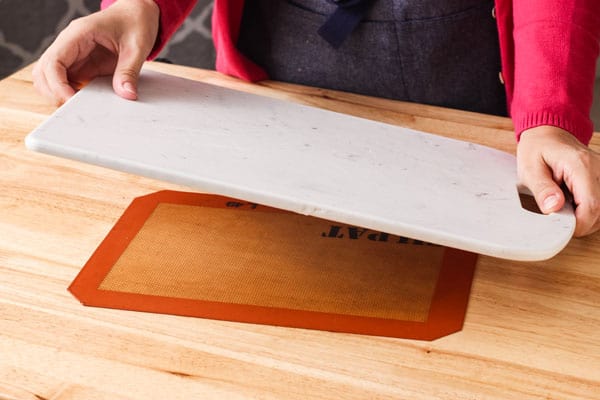 Person holding a cutting board over a baking mat on a table.