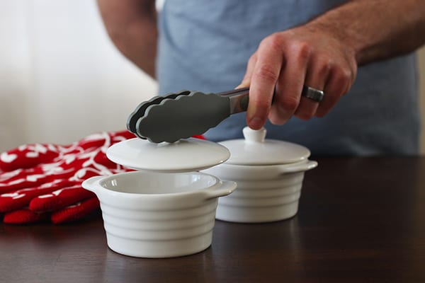 tongs lifting lid off of white mini cocottes