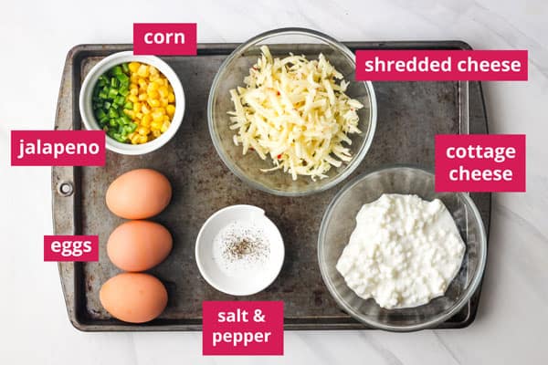 Eggs, cottage cheese, shredded cheese, corn, jalapeno, and seasonings labeled on a sheet pan.