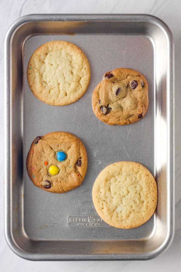 Four baked sugar and chocolate chip cookies on an eighth sheet pan.