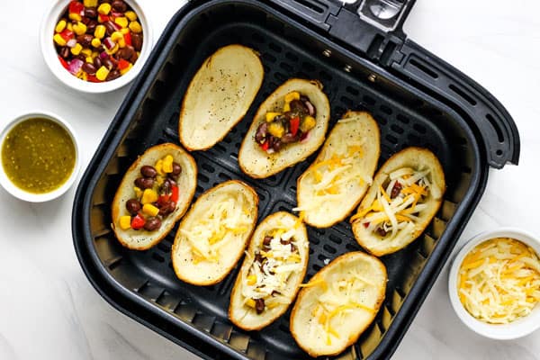 Filled potato skins in an air fryer next to ramekins of cheese and salsa.