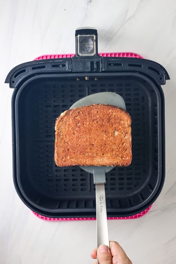 Hand lifting toasted sandwich with a large spatula.