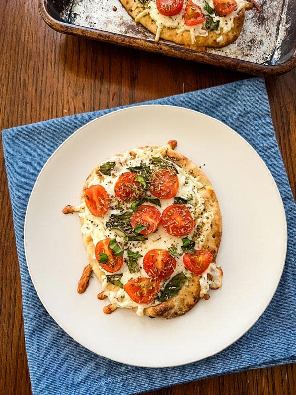 Cheesy mini tomato and basil flatbread on a plate.