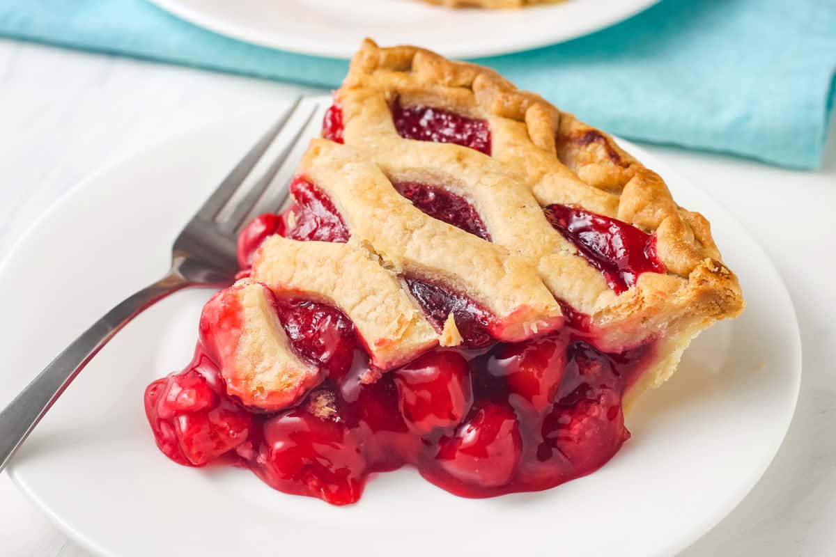 Closeup of cherry pie slice with golden crust and a juicy filling spilling out of it.