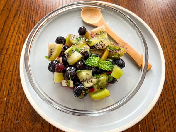 Smal bowl of chopped kiwi, blueberries, and mint with a small spoon.