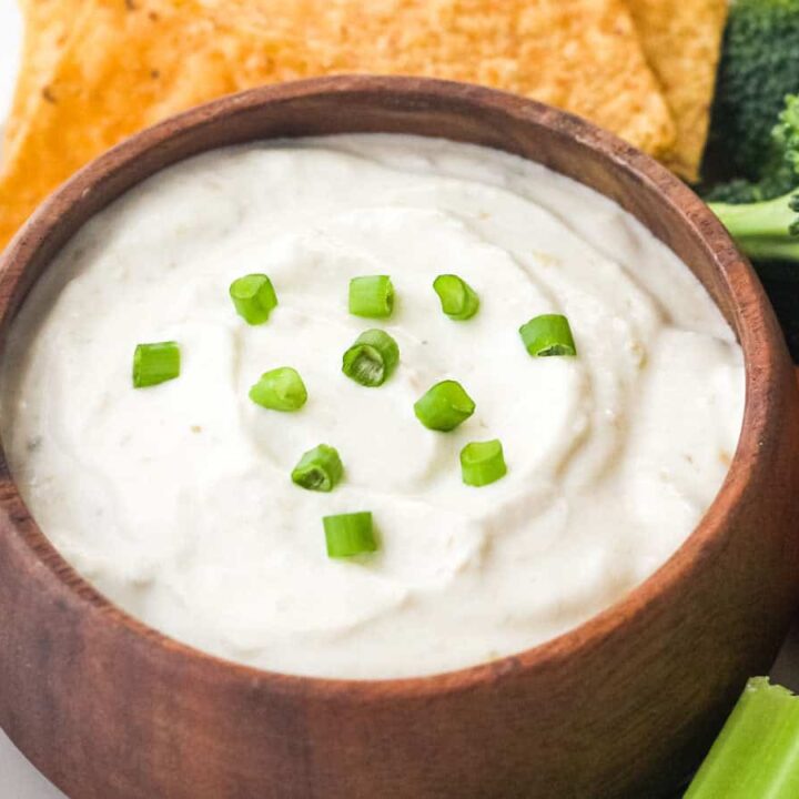 Small wooden bowl filled with dip and topped with sliced green onion.