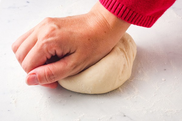 Closeup of hand kneading a small ball of bread dough.