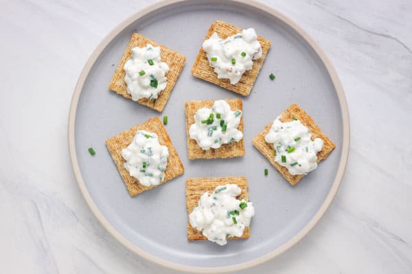 A plate of wheat crackers topped with cottage cheese and fresh chives.