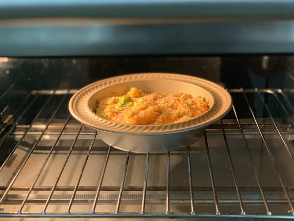 Frozen mac and cheese in a mini pie plate cooking inside a toaster oven.