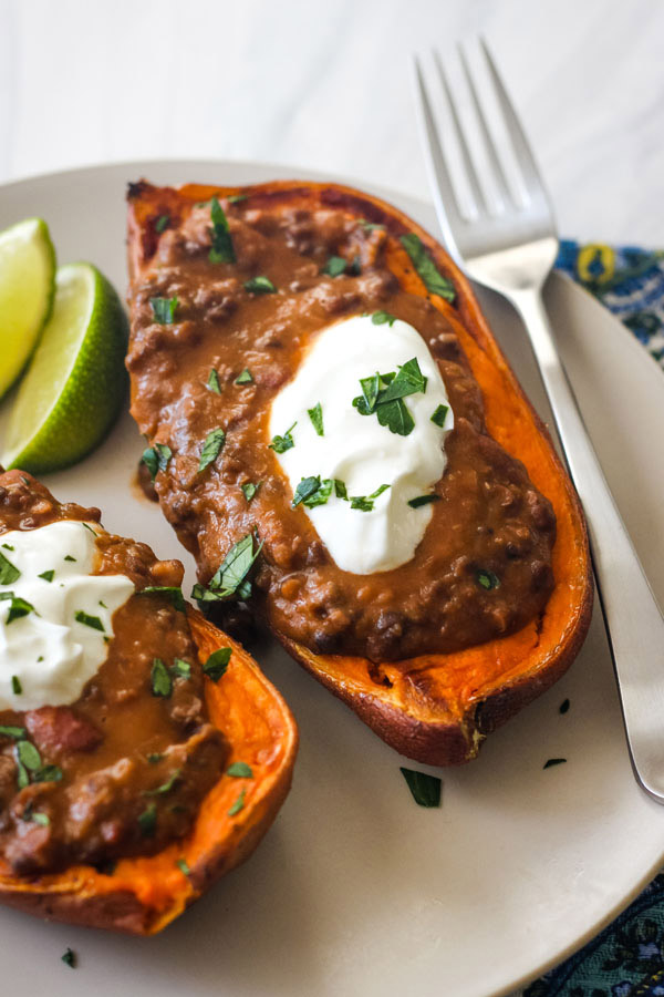 A plate with a fork and half a sweet potato topped with lentils and yogurt.