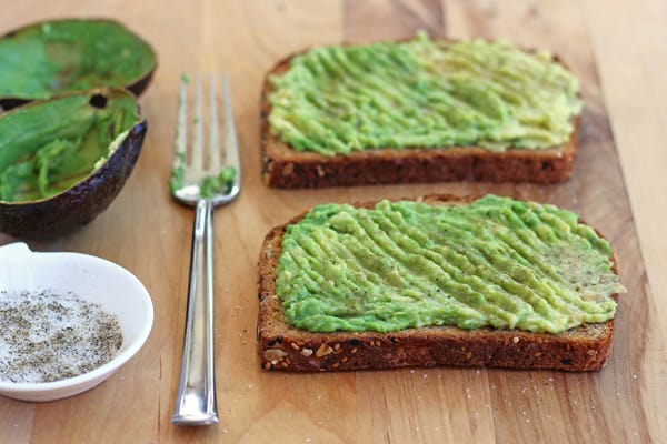 Toast with mashed avocado next to a fork and empty avocado skins.