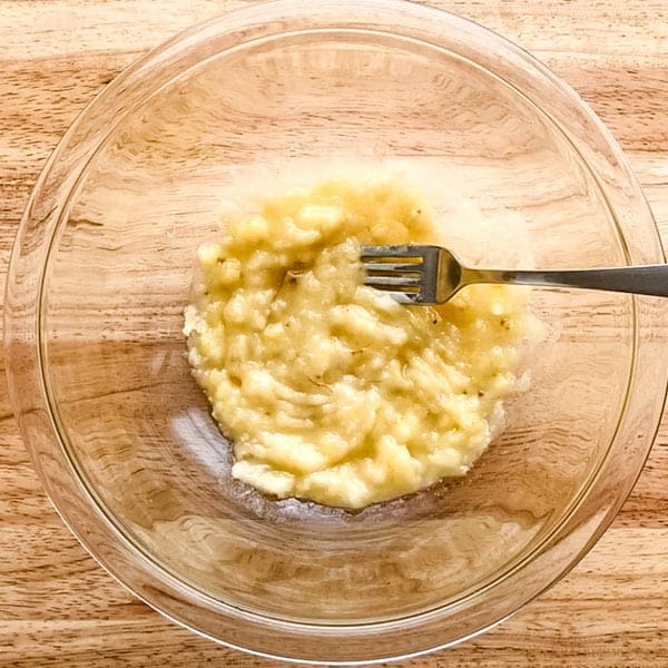 Overhead view of banana mashed in a bowl with a fork.