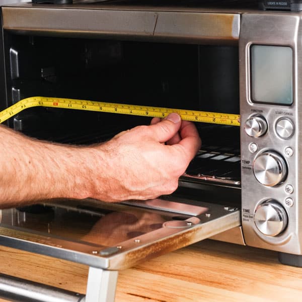 Man holding measuring tape inside of toaster oven.