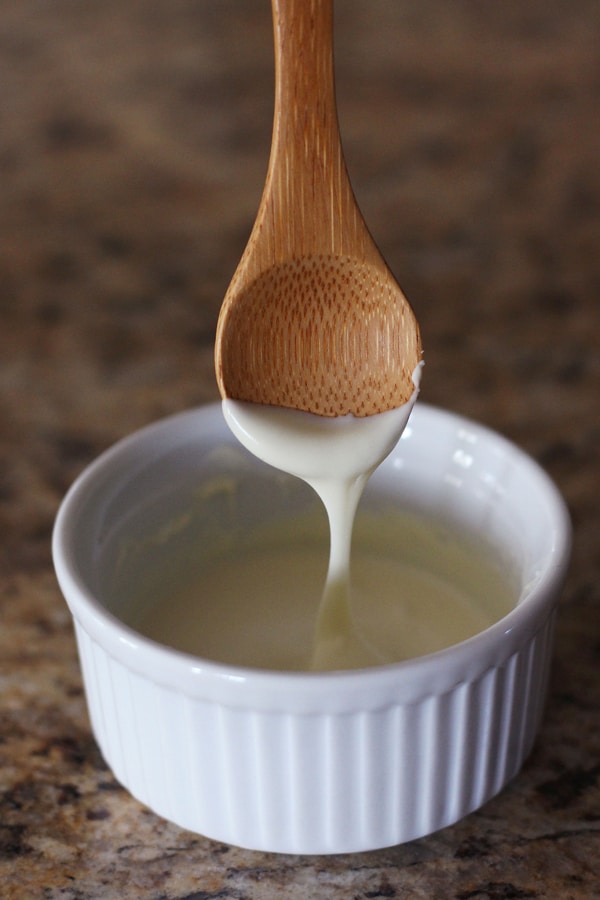 Melted white chocolate dripping from a wooden spoon.