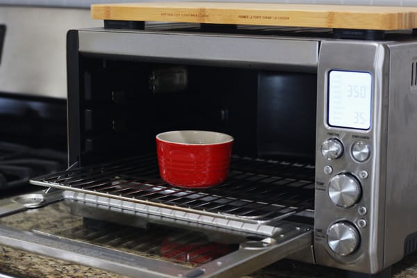 A small red ramekin with chocolate chips in a toaster oven.