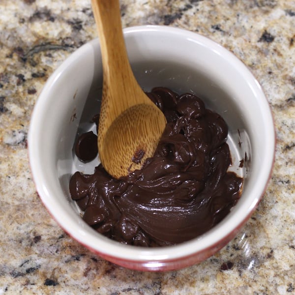 Partially melted chocolate chips in a ramekin with a spoon.