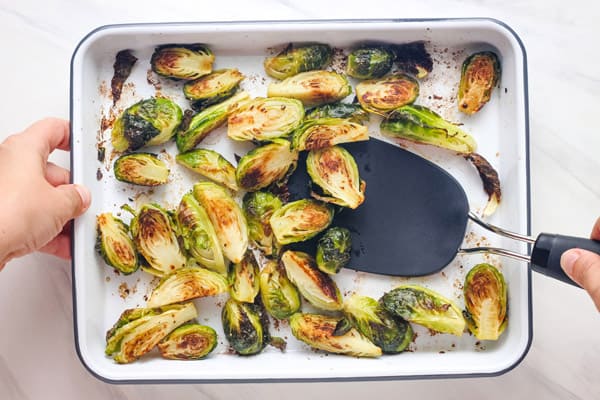 Overhead view of roasted Brussels sprouts tossed with a black spatula.