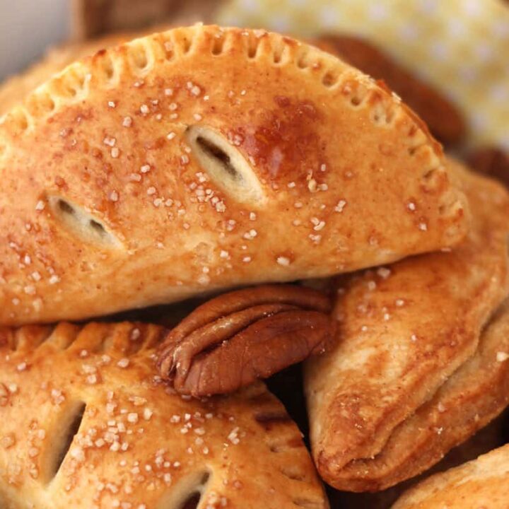 Closeup of golden brown mini hand pies and whole pecans in a bowl.