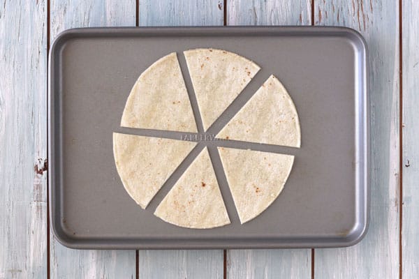 Wedges of oiled and seasoned corn tortilla on a toaster oven baking sheet.