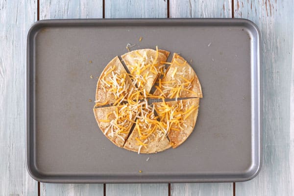 Tortilla chips with shredded cheese on a toaster oven baking sheet.