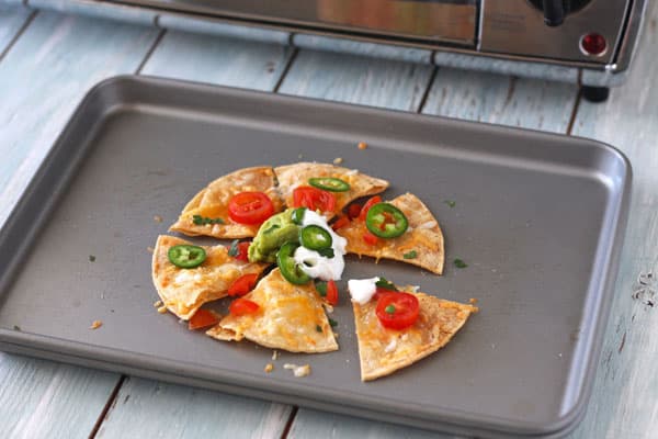 Single serving of nachos on a baking sheet in front of a toaster oven.